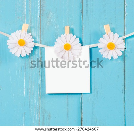 Chamomile flower clothespins with blank paper on blue wood background