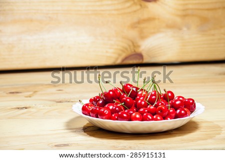Red sweet cherry in a plate on a wooden table from boards, nobody.