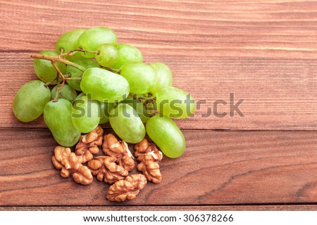 White grapes of green color and walnut on a wooden table from boards.