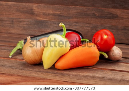 Vegetables on a wooden table from brown boards, vegetarian healthy food, paprika, onions, an eggplant, potato, tomato.