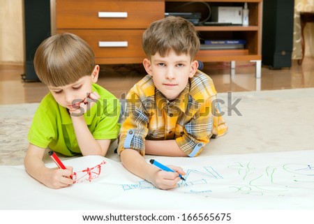 Two boys draw on big white list of paper