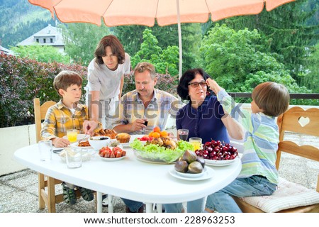 The family from five persons have got dinner on summer terrace in sunny day