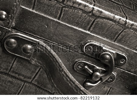 Warm toned black and white close up of small case showing metal clasp and leather handle