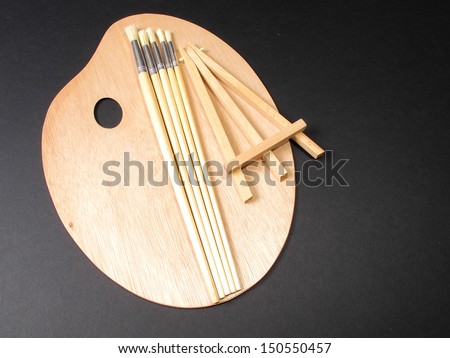 An image of paint brushes and an Easel laying on a painters pallette / Artists things
