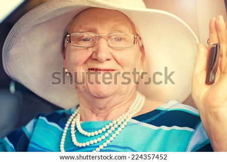 senior smiling woman in glasses sitting in a car and holding automobile key