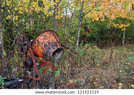 An old cement mixer over grown by nature sits in a fence row