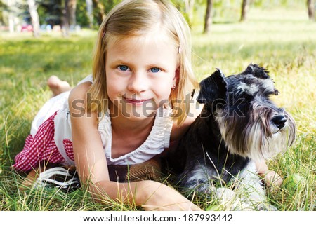 smiling little girl hugging her dog lying on green grass in summer day