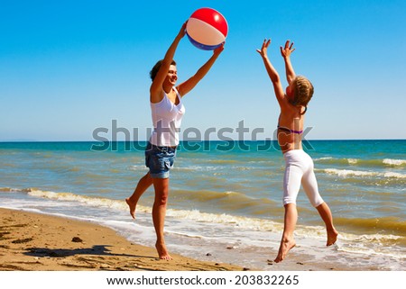 Mom and daughter play with a ball on the ocean shore on a sunny day in summer