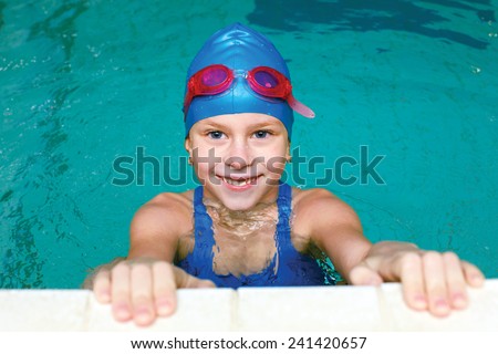 beautiful girl in a bathing suit, swim cap, goggles, holding on overboard in a swimming pool