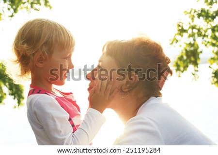 cute little daughter gently stroking her mother\'s face. mother and daughter looking at each other\'s eyes
