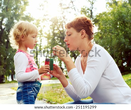happy mother and her daughter blowing soap bubbles on a warm summer day