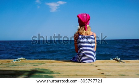 Girl in a striped dress looks at the blue sea. Girl sitting alone on the wooden pier. Seascape. Lifestyle.