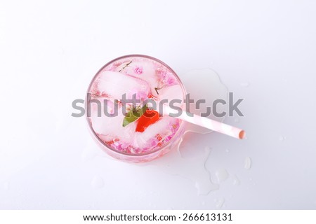 Ice cubes with pink flowers in glass  with paper straw on white background