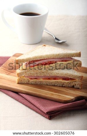 fresh sandwich with ham, cheese and tomato on wooden board
with coffee for breakfast