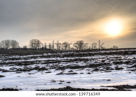 Sunrise on a calm early spring morning with a barren field and trees ind the horizon.