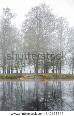 Boat and canoe on the edge of a lake shrouded in morning fog.
