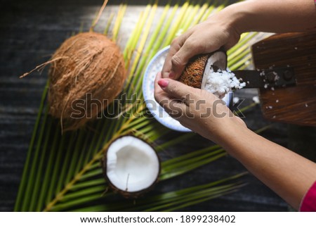 Woman sit on coconut grater to grate coconut into bowl palm leaf background Kerala India. make coconut milk Home by squeezing for cooking curry, virgin coconut oil.