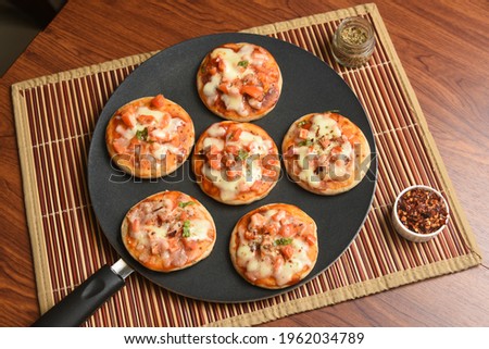 Many Mini Pizza, Fresh homemade Tawa pizzas , pan pizza cooked with mozzarella cheese, parsley, cherry tomato and basil on rustic wooden background . Vegetarian wheat pizza Mumbai India. Indian food