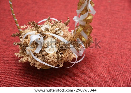 Basket full of dried flowers with white and golden ribbon isolated on red jute background. Wedding flower basket.Decoration bouquets of dried flowers.DRIED FLORAL BOUQUET IN A BASKET