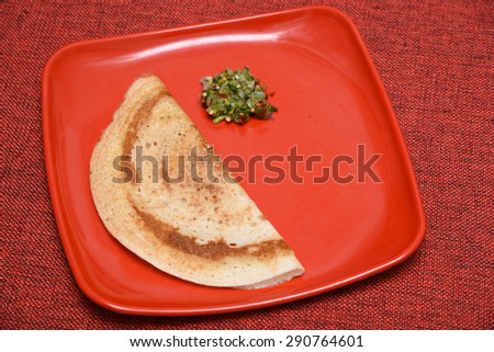 Dosa with green chutney in a red plate, south Indian breakfast. On red background\
a fermented crepe made from rice batter and black lentils.staple dish in states of Karnataka, Tamil nadu, Kerala.