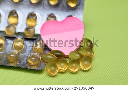 Cod liver fish oil omega 3 gel capsules isolated on green background. heart shaped paper copy space for text. metal foil blister strip packaging.nutritional supplement  contains Vitamin A, Vitamin D