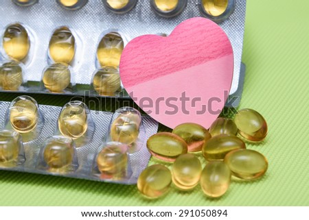 Cod liver fish oil omega 3 gel capsules isolated on green background. heart shaped paper copy space for text. metal foil blister strip packaging.nutritional supplement  contains Vitamin A, Vitamin D
