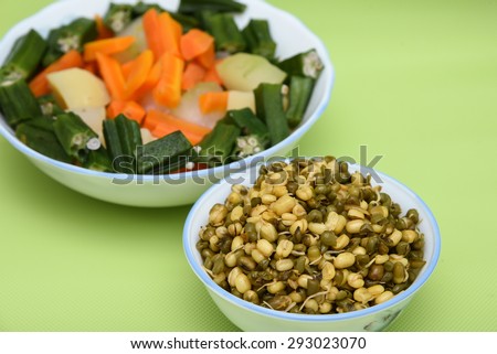 fresh vegetables carrot ladies finger potatoes cut up slices in bowls and sprouted seeds of green gram isolated on green
