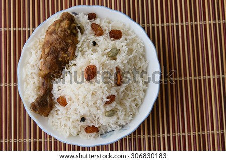 Chicken Biryani  or fried rice with fired chicken leg in white bowl on a bamboo mat .closeup view of delicious Indian chicken biriyani with colorful garnish, served with raita or curd.