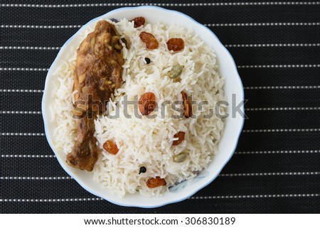 Chicken Biryani  or fried rice with fired chicken leg in white bowl on a black background  .closeup view of delicious Indian chicken biriyani with colorful garnish, served with raita or curd.