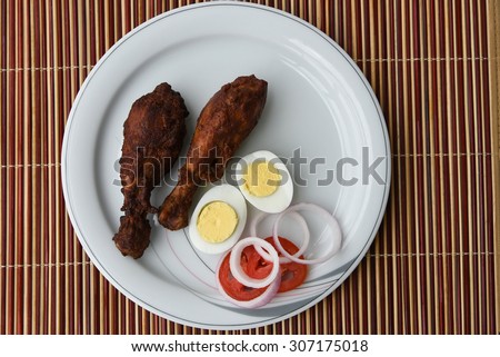 Delicious Grilled chicken legs with eggs, onion rings and tomatoes served on a white plate on a bamboo mat background. Tasty Roasted chicken drumstick with boiled egg halves and vegetables.chicken fry