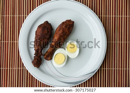 Delicious Grilled chicken legs with eggs served on a white plate on a bamboo mat background. Tasty Roasted chicken drumstick with boiled egg halves.chicken fry and egg white, yolk of egg