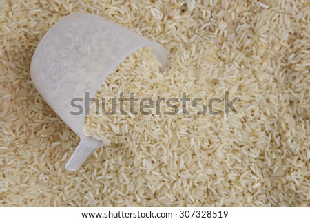 measuring cup filled with raw white rice with rice as background. basmati or jasmine rice used to prepare biriyani or pulav in India.uncooked long grain rice. grains falling from measuring cup