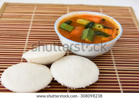 Indian vegetarian rice cakes breakfast known as idli or idly, served with sambar in a bowl on bamboo mat background.delicious South India dish contain carrot potato,ladies finger ,drum stick,tomato