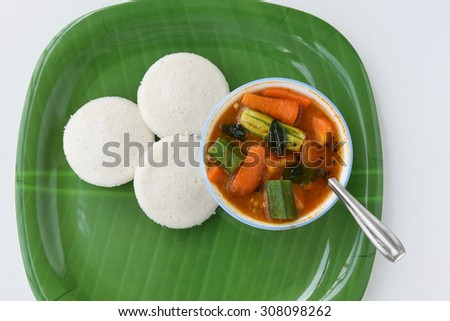 Indian vegetarian rice cakes breakfast known as idli or idly, served with sambar in a bowl spoon on green plate on bamboo mat background.delicious South India dish contain carrot potato,ladies finger