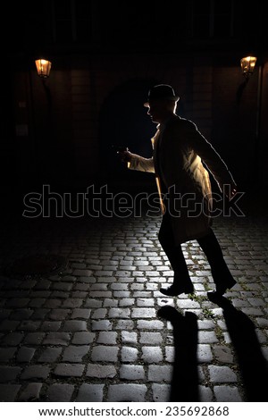 Gangster wearing a classic trench coat. The man is running on cobblestone with a gun in his hand. The light creates a long shadow towards the viewer. Image inspired by \