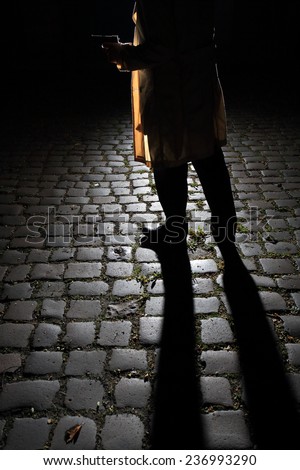 Gangster holding a gun. Only the lower part of the body is visible. Light from the back creates a long shadow and silhouette. Image inspired by \