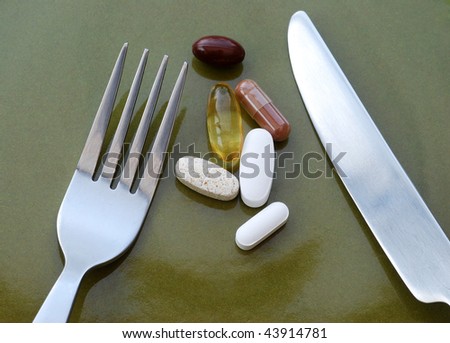 Vitamin pills and capsules on plate with knife and fork