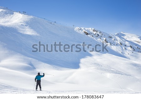 Lone skier waving on a snowy mountain peak covered in pristine fresh white powder as he or she prepares to descend the ski run in a beautiful cold sunny winter landscape