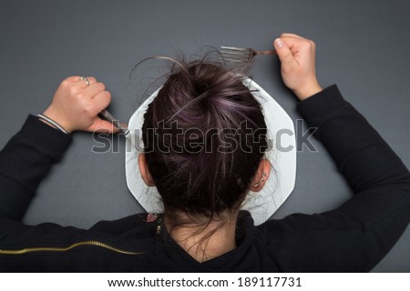 Girl is watching her plate while holds her fork and knife. Gray slate background.