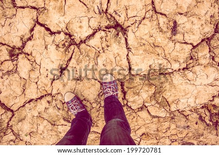 background feet in sneakers and jeans standing on dry soil with cracks