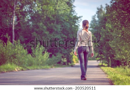 background girl standing turned her back on urban asphalt road  among trees and tall grass outside the town