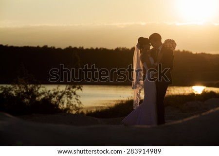 Groom and bride is hugging and kissing on the background beautiful sunset on the lake