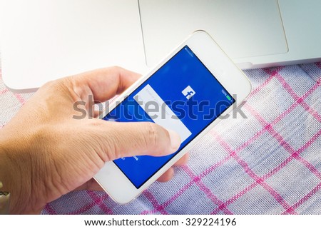 SUKHOTHAI ,THAILAND - OCTOBER 19, 2015: Young man touch Facebook login icons on Smartphone. Facebook is largest and most popular social networking site in the world.