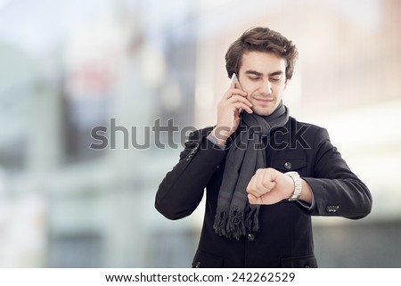 Young businessman talking on mobile phone and  looking at watch on street