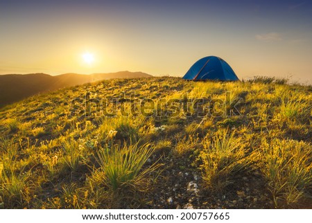 Sunrise in a high mountain valley with touristic travel tent on a hill