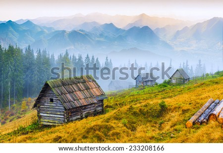 Sunrise above the high mountain foggy valley with old wooden houses on a hill in a mountain forest.