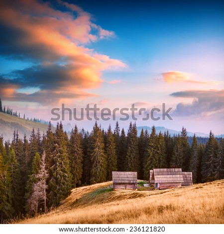 Sunrise above the high mountain foggy valley with old wooden houses on a hill