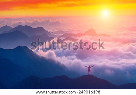 Man standing on a mountain top with raised hands and welcome sunrise in a Crimea mountains above the cloudy valley
