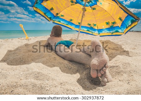 Little kid with feet in send lying on a sandy beach under umbrella