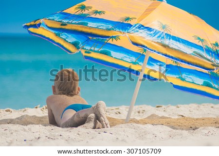Little kid lying on a sandy beach under umbrella
